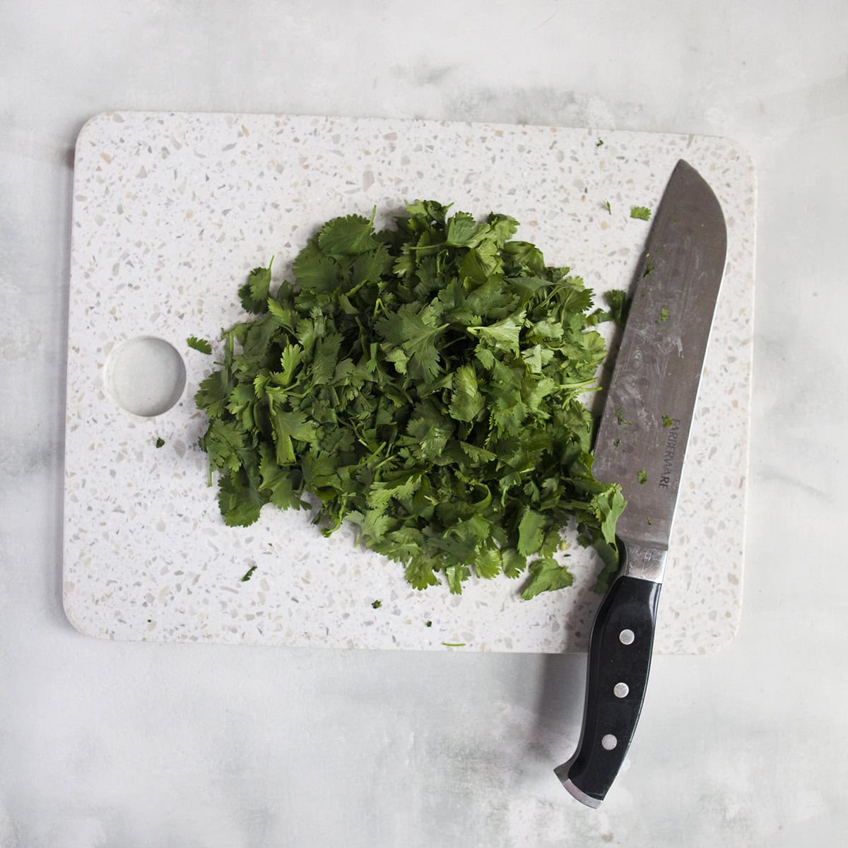 Chopped cilantro on a cutting board next to a knife on a gray background.