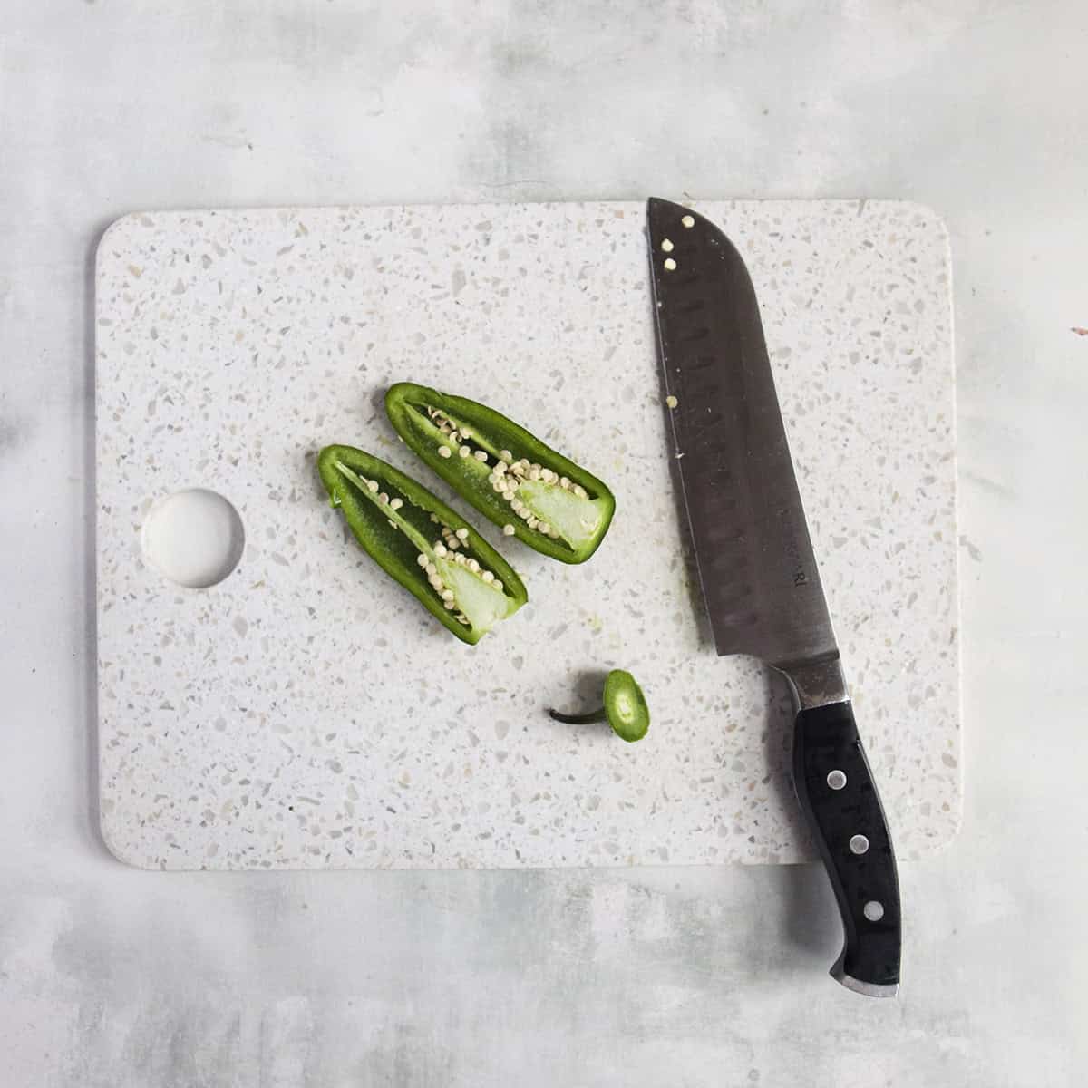 Jalapeno sliced in half on a cutting board next to a knife on a gray background.