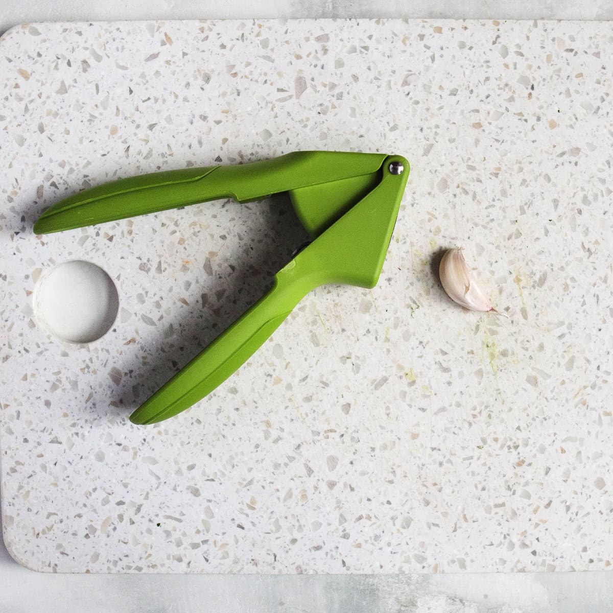 Garlic clove next to a green garlic press on a cutting board.