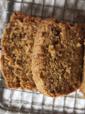 Golden brown homemade chai-spiced banana bread loaf with two slices resting on a wire grater on top of a white dish towel.