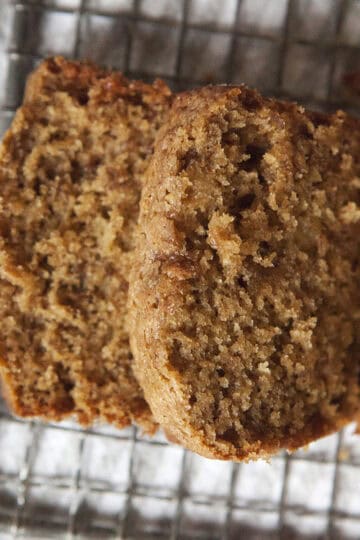 Golden brown homemade chai-spiced banana bread loaf with two slices resting on a wire grater on top of a white dish towel.