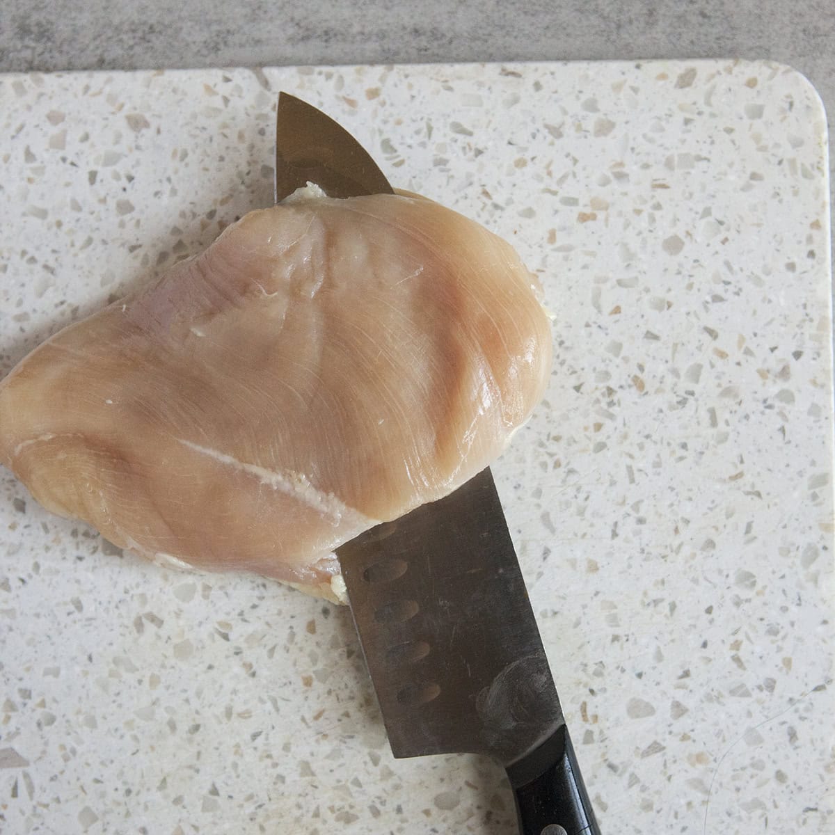 A raw chicken breast being sliced on a cutting board.