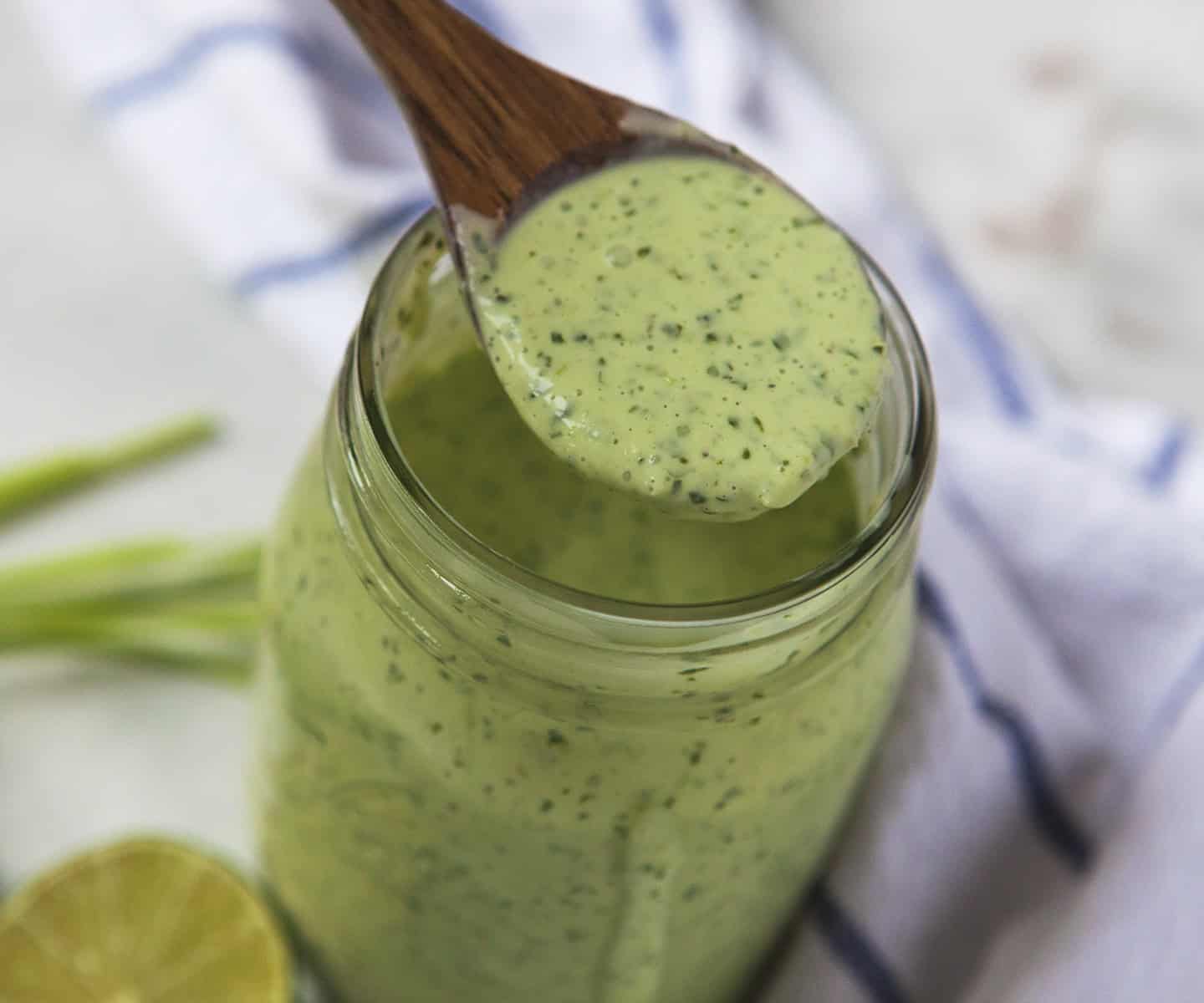 Creamy jalapeno ranch dressing on a wooden spoon above a mason jar full of dressing.