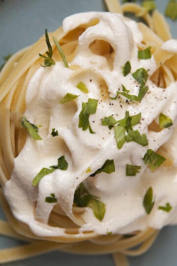 Thick, creamy Alfredo sauce on a nest of fettuccine, topped with chopped parsley and pepper, on a blue plate.