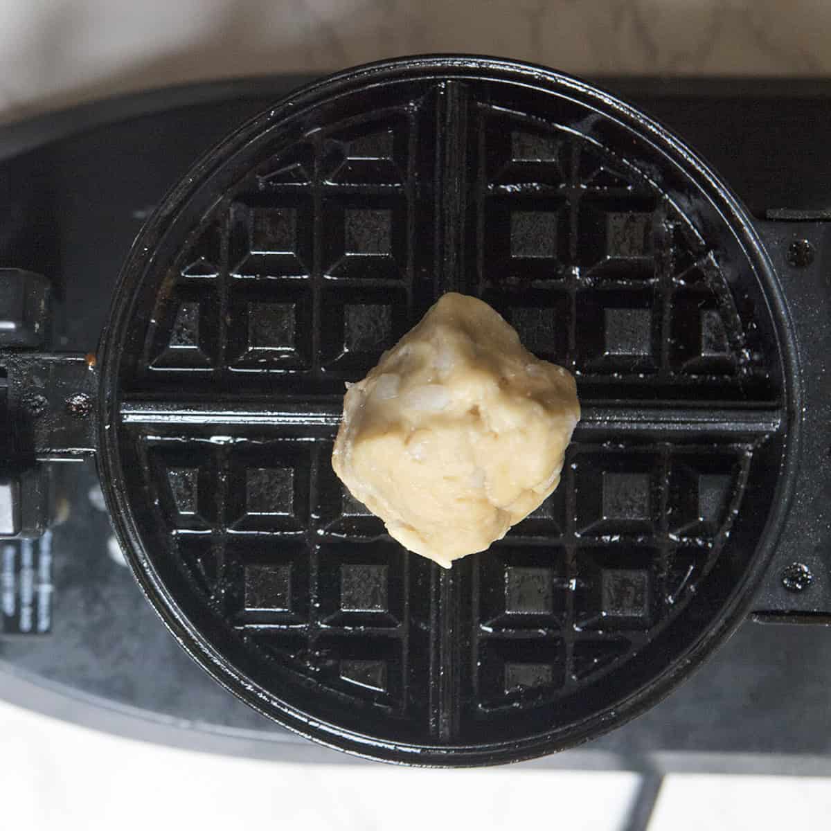 A ball of Belgian Liege waffle dough on a Belgian waffle iron.