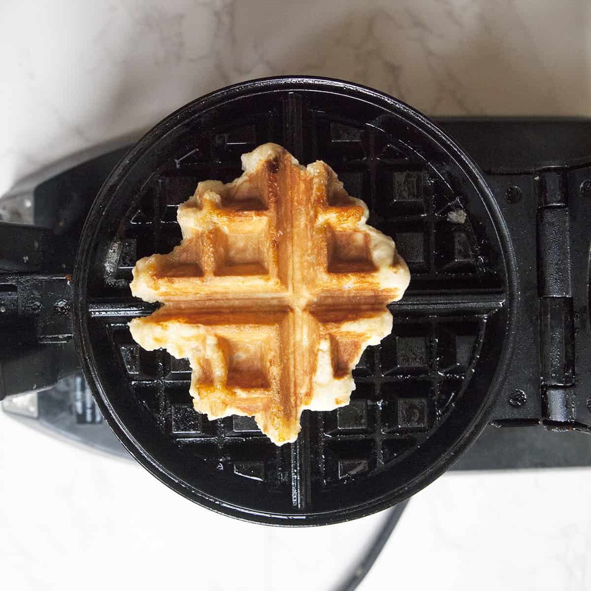 A golden brown, cooked Belgian Liege waffle on a black waffle iron.