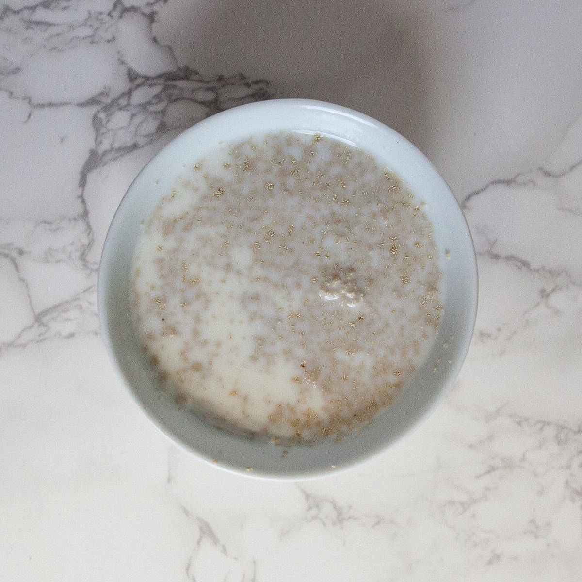 Yeast and milk mixture in a small bowl on a white marble countertop.  Yeast is slightly bubbly.