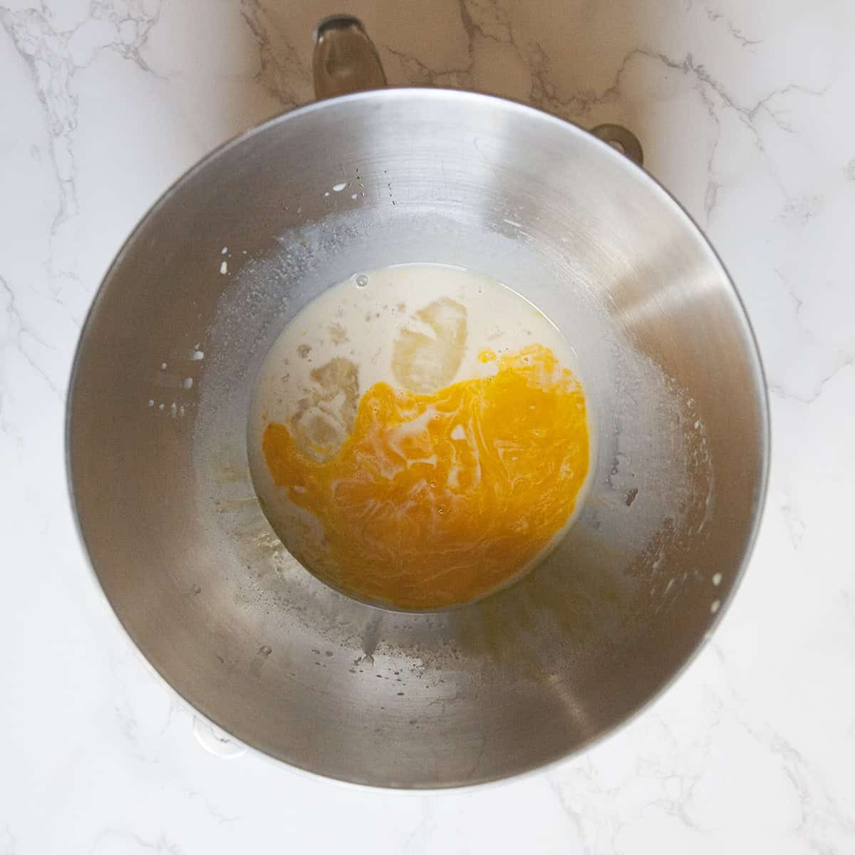 Ingredients for Belgian Liege waffles in the bowl of a stand mixer on a white marble countertop.