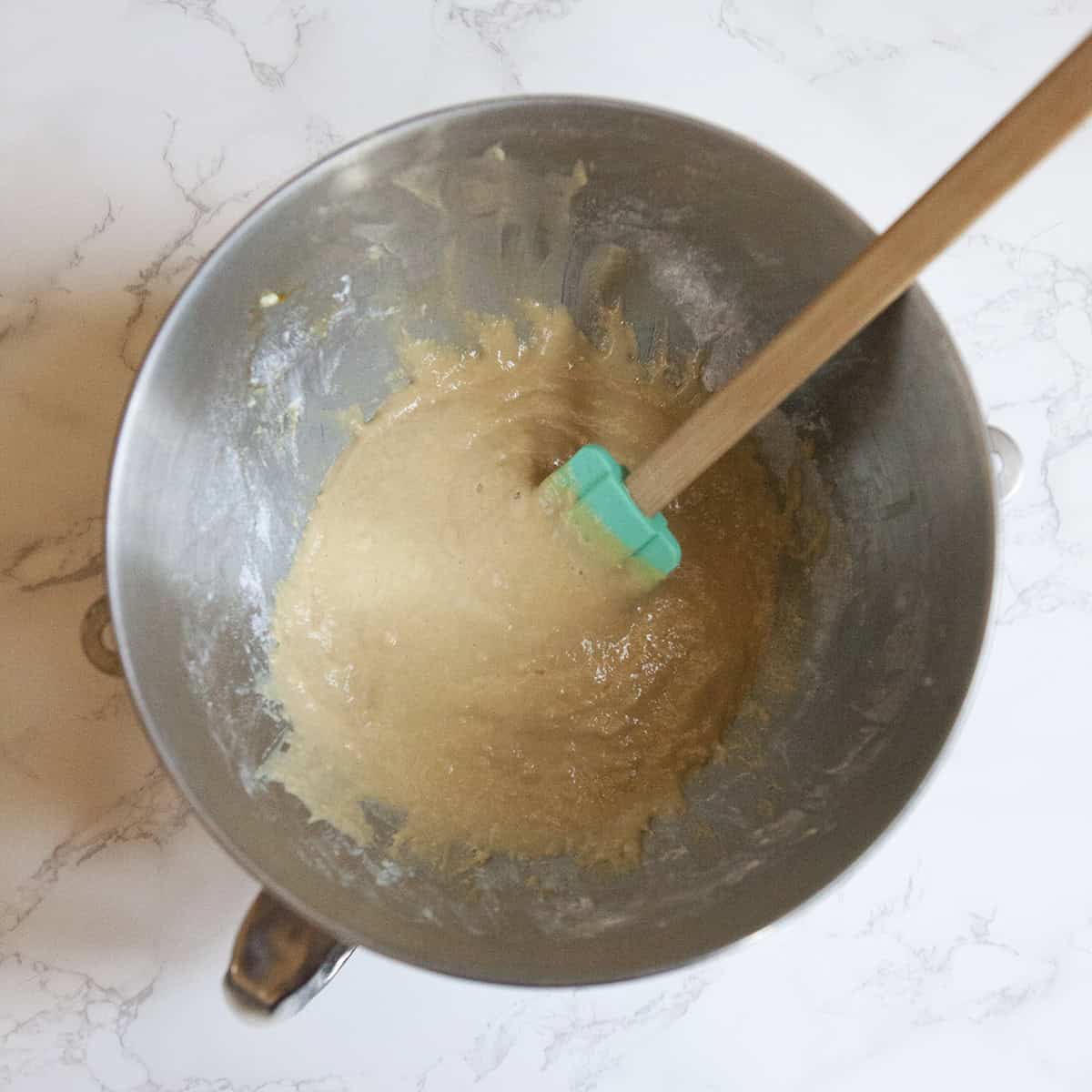 Dough for Belgian Liege waffles in the bowl of a stand mixer on a white marble countertop with a spatula.