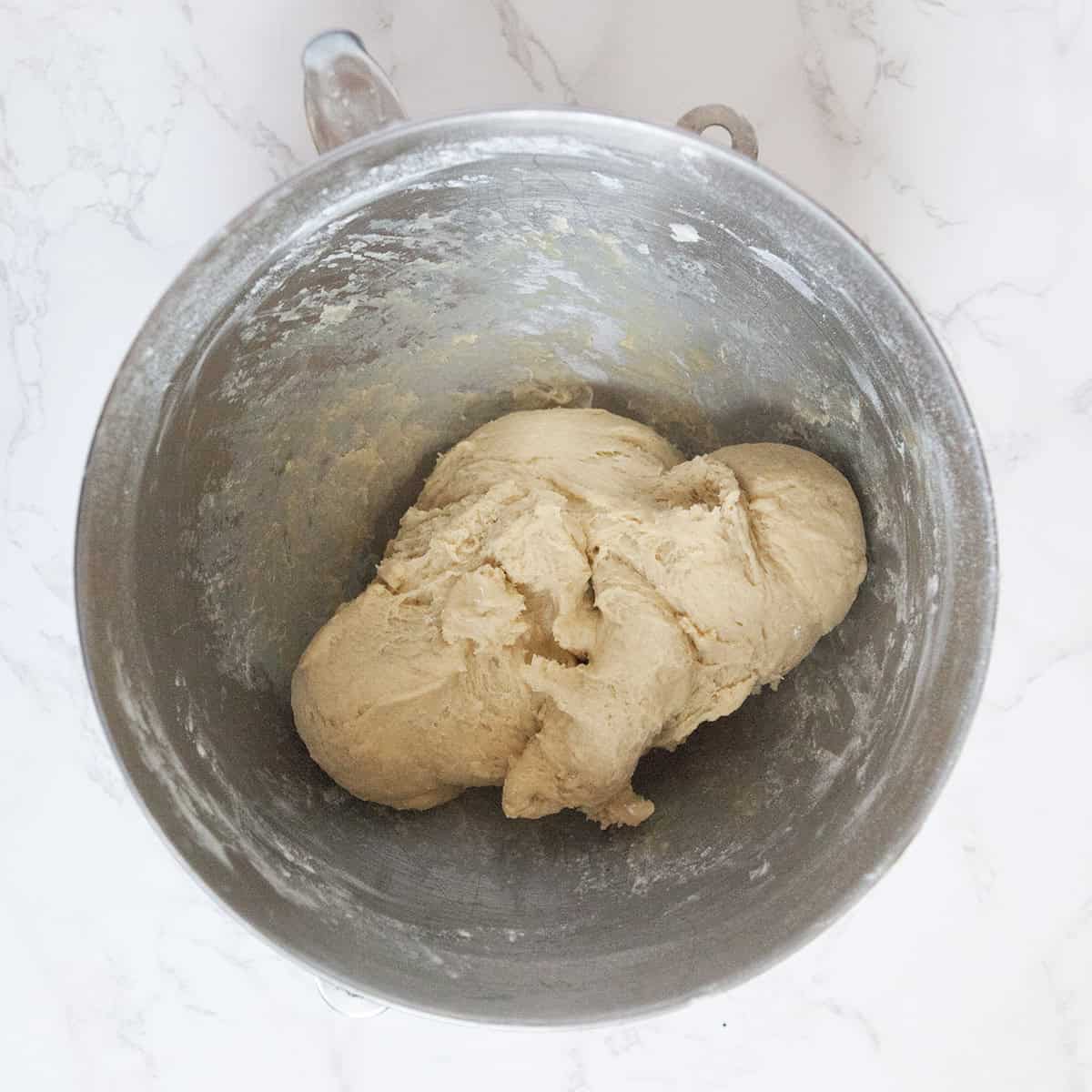 Belgian Liege waffle dough in the bowl of a stand mixer on a white marble countertop.