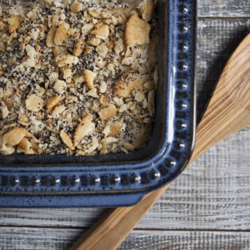 Poppy seed chicken casserole in a blue baking dish with a wooden spoon on a whitewashed wooden table.