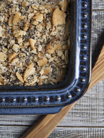 Poppy seed chicken casserole in a blue baking dish with a wooden spoon on a whitewashed wooden table.