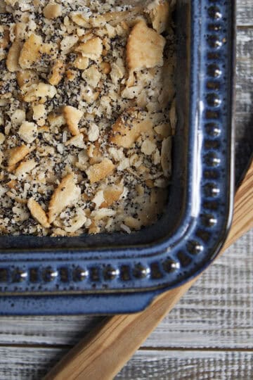 Poppy seed chicken casserole in a blue baking dish with a wooden spoon on a whitewashed wooden table.