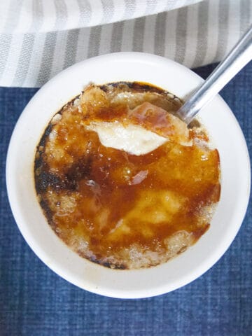 Chai-spiced creme brulee in a white ramekin with a caramelized sugar top, with a spoon, on a blue background with a gray napkin.