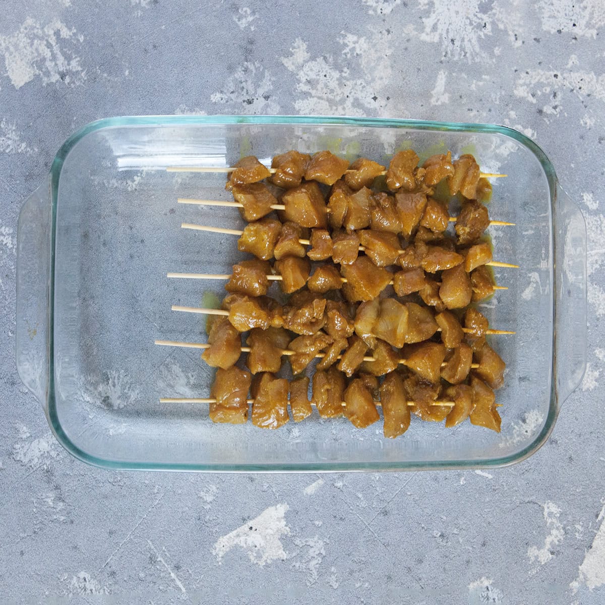 Marinated Thai-style chicken satay skewers in a baking dish on a gray background.