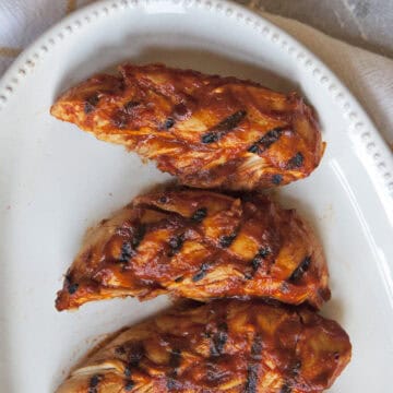 Grilled chicken tenders covered in barbecue sauce on a white plate.