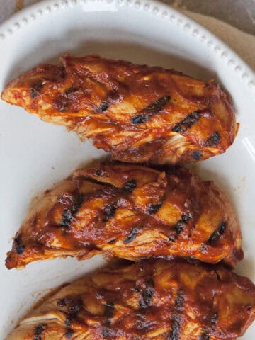 Grilled chicken tenders covered in barbecue sauce on a white plate.