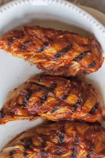 Grilled chicken tenders covered in barbecue sauce on a white plate.