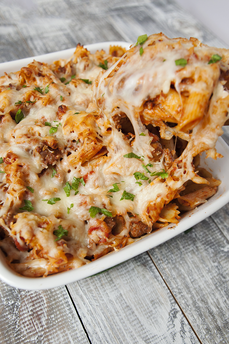 Pepperoni pasta bake with Italian sausage and mozzarella topped with chopped parsley being spooned out of a white baking dish.