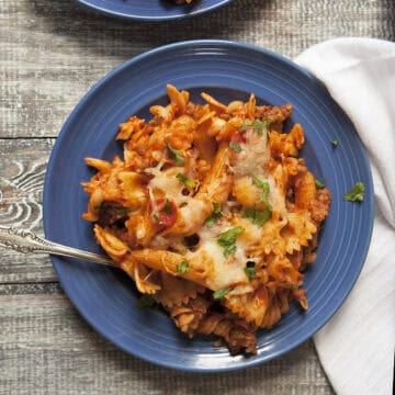 Pepperoni and Italian sausage pasta bake with red sauce on a blue plate next to a white napkin on a wooden table.