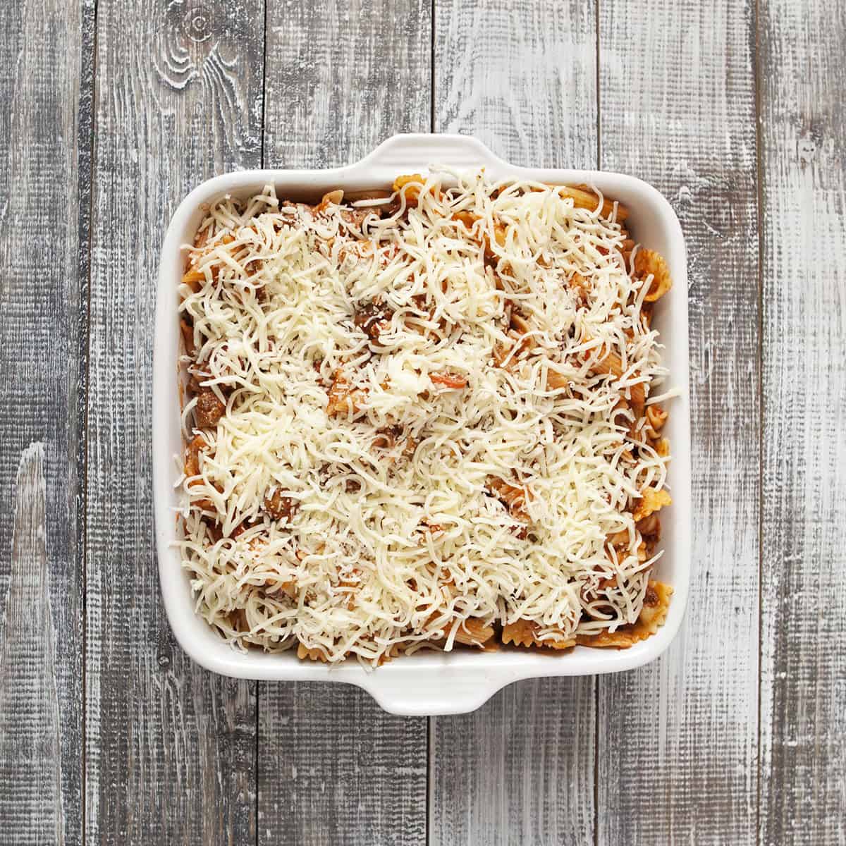 Pepperoni pasta bake topped with mozzarella in a square white baking dish.