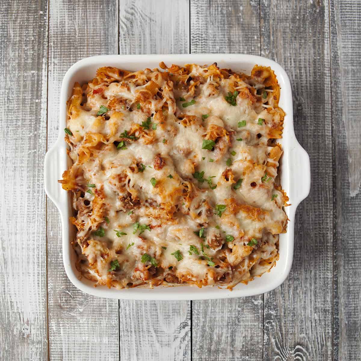 Cooked pepperoni pasta bake topped with melted mozzarella cheese and chopped parsley in a square white baking dish.