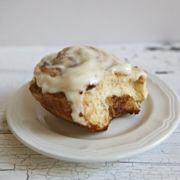 Soft and fluffy cinnamon roll with cream cheese frosting on a white plate