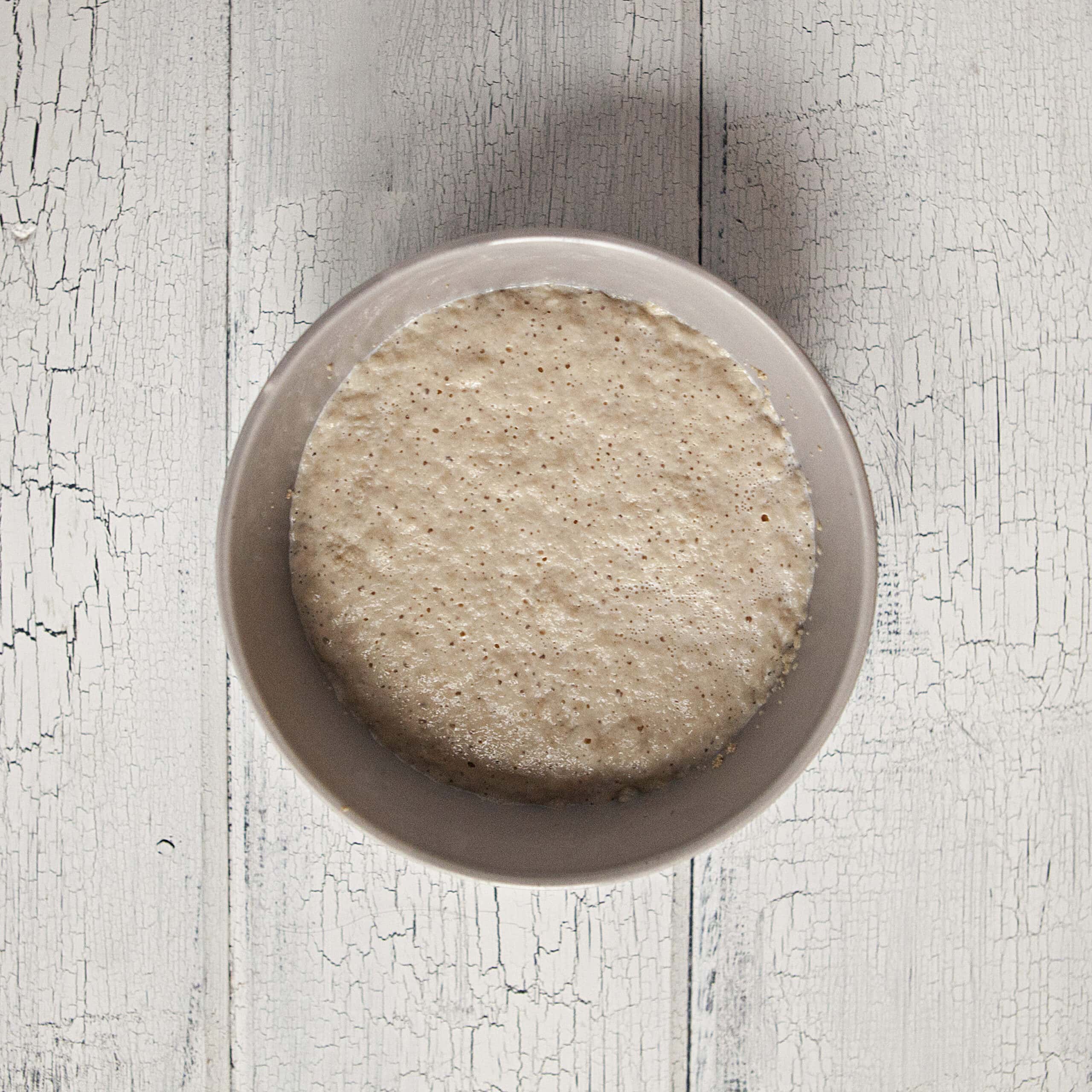 Foamy yeast in a gray bowl on a white wood background.