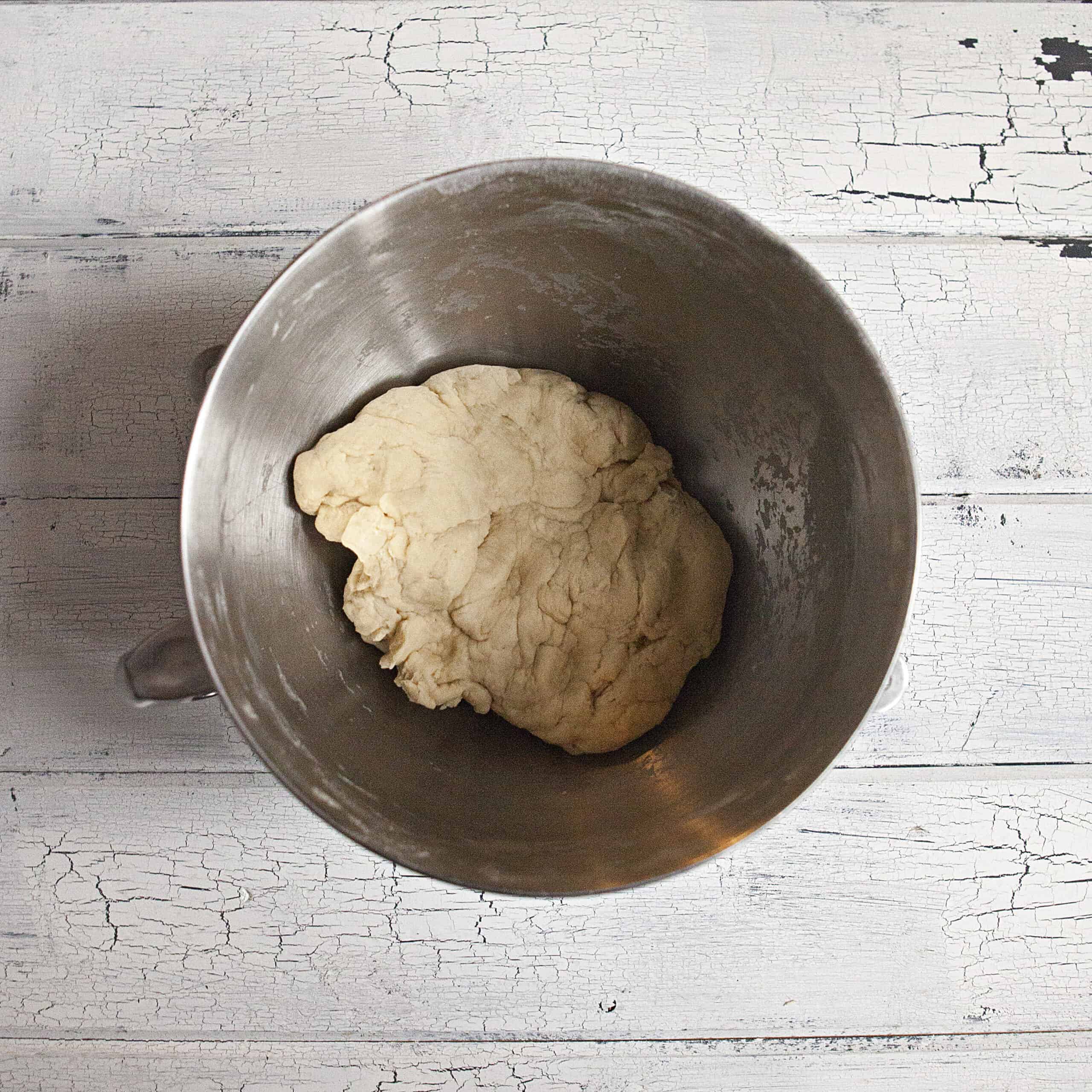 Dough for soft and fluffy cinnamon rolls in the metal bowl of a stand mixer on a white wood background.