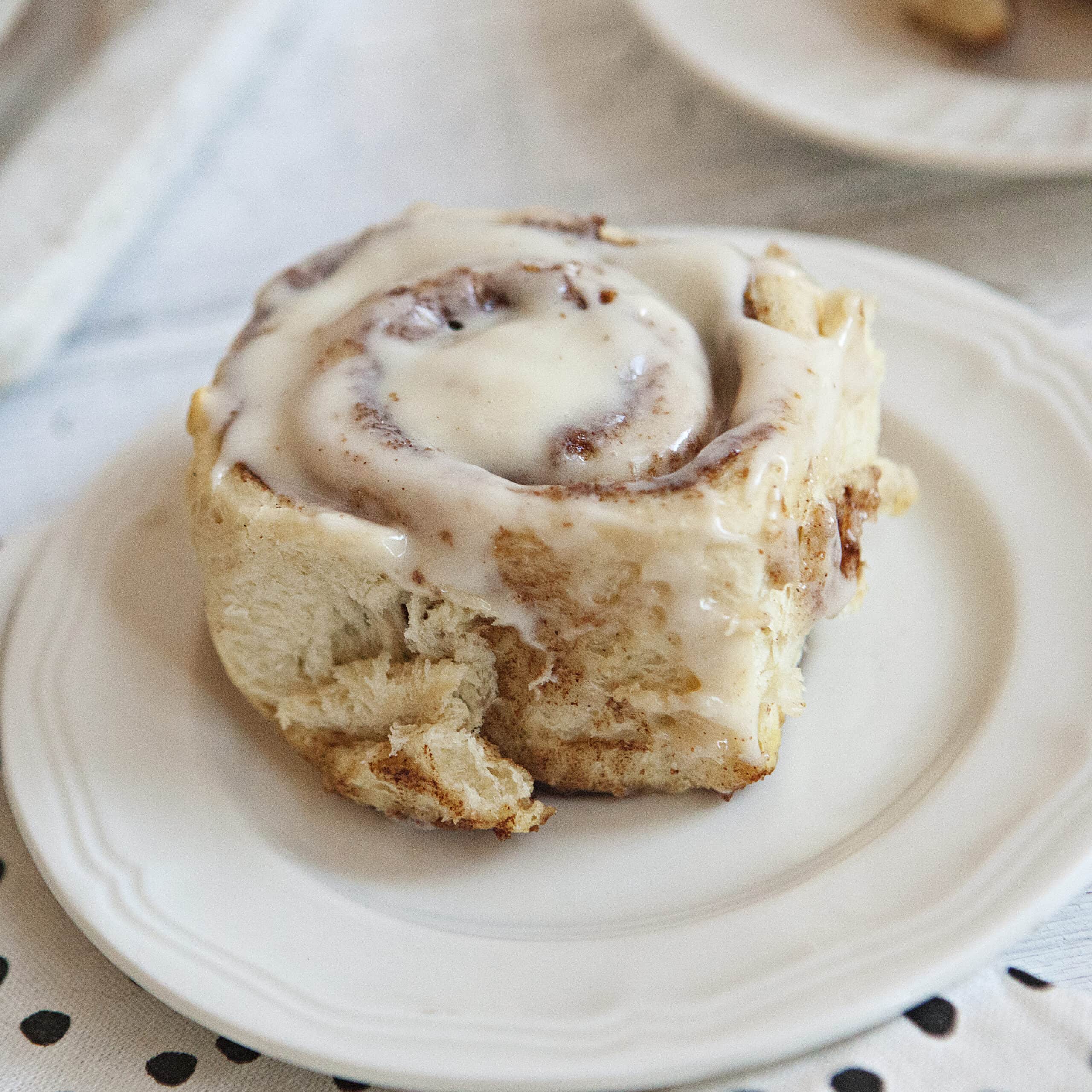 Soft and fluffy cinnamon roll with cream cheese frosting on a white plate