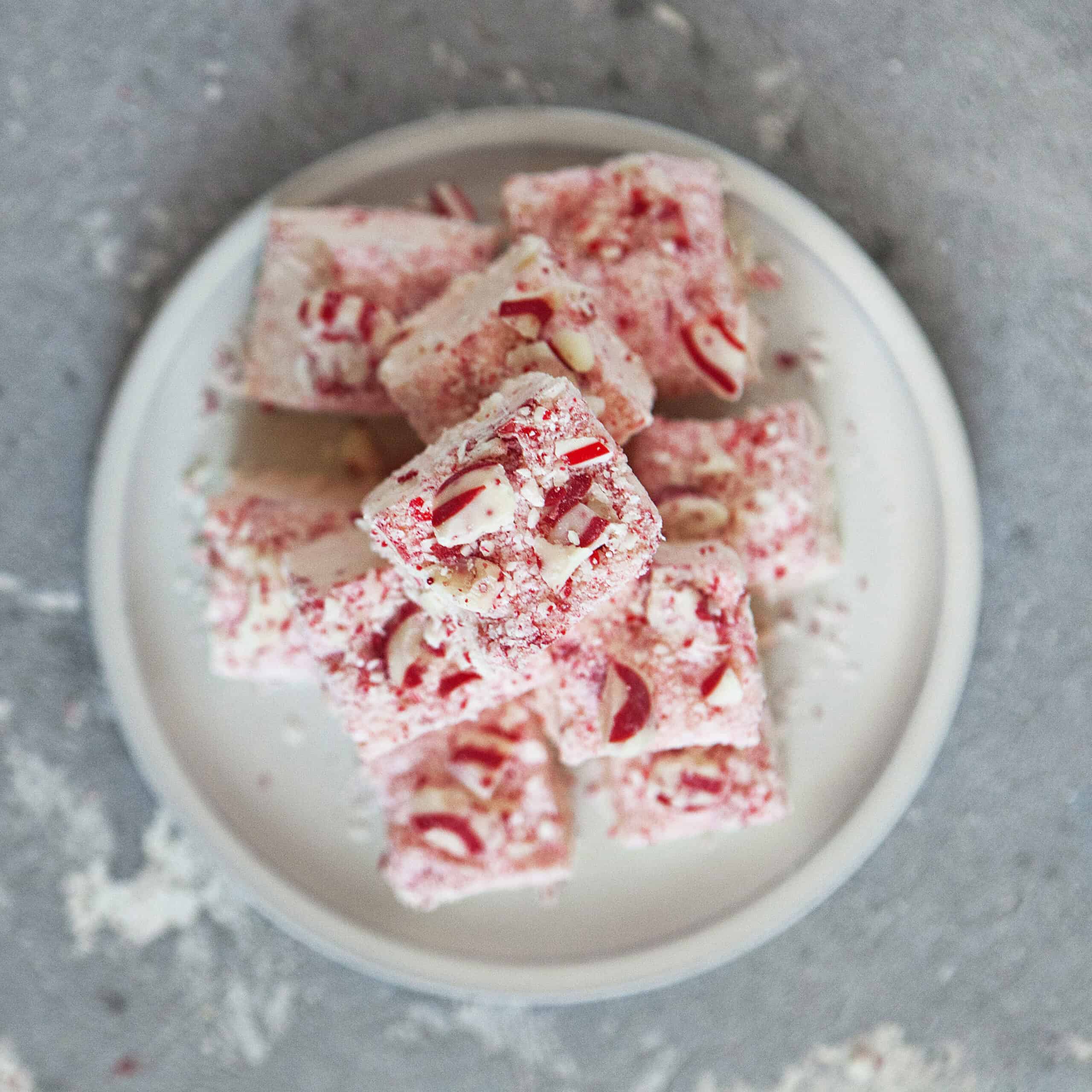 A pyramid of pink, red, and white chocolate candy cane crunch fudge on a white plate on a gray background.