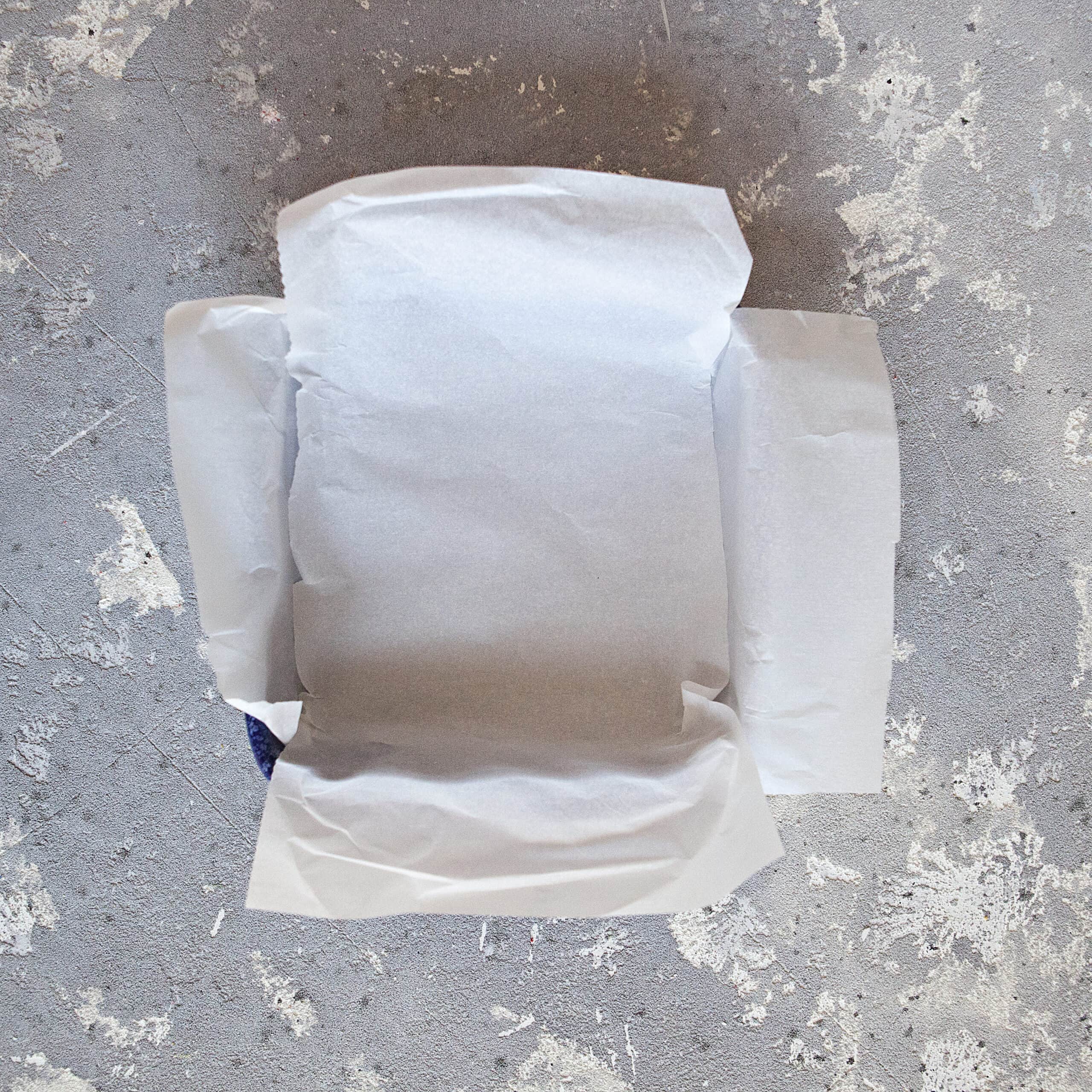 A 9x9-inch baking dish lined with two pieces of parchment paper on a gray background.