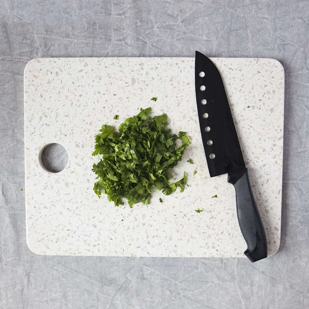 Chopped cilantro on a white cutting board with a black chef's knife on a gray background.