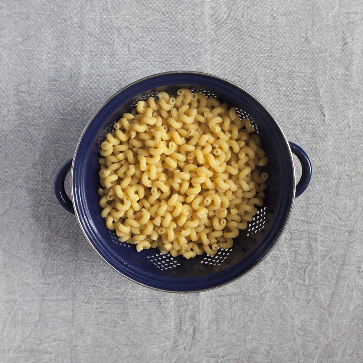 Cooked fusilli pasta in a navy blue colander on a gray background.