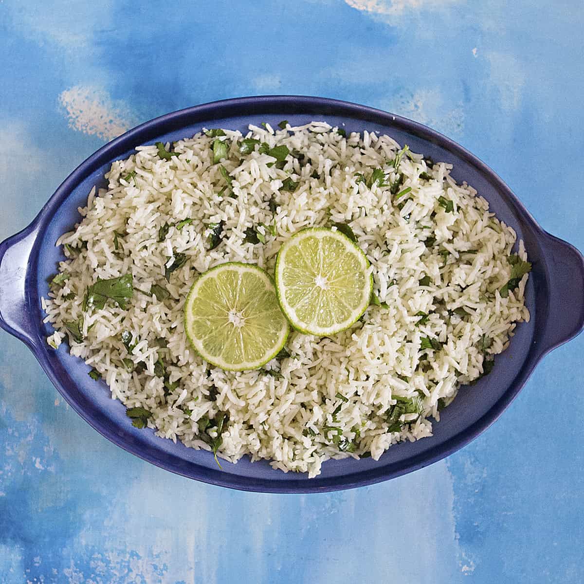 Fluffy cilantro-lime rice in a blue serving dish topped with lime slices on a blue background.