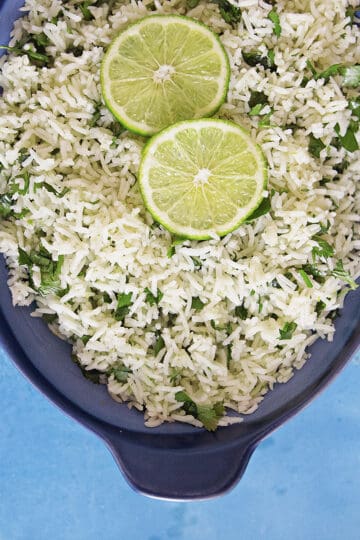 Fluffy cilantro-lime rice in a blue serving dish topped with lime slices on a blue background.