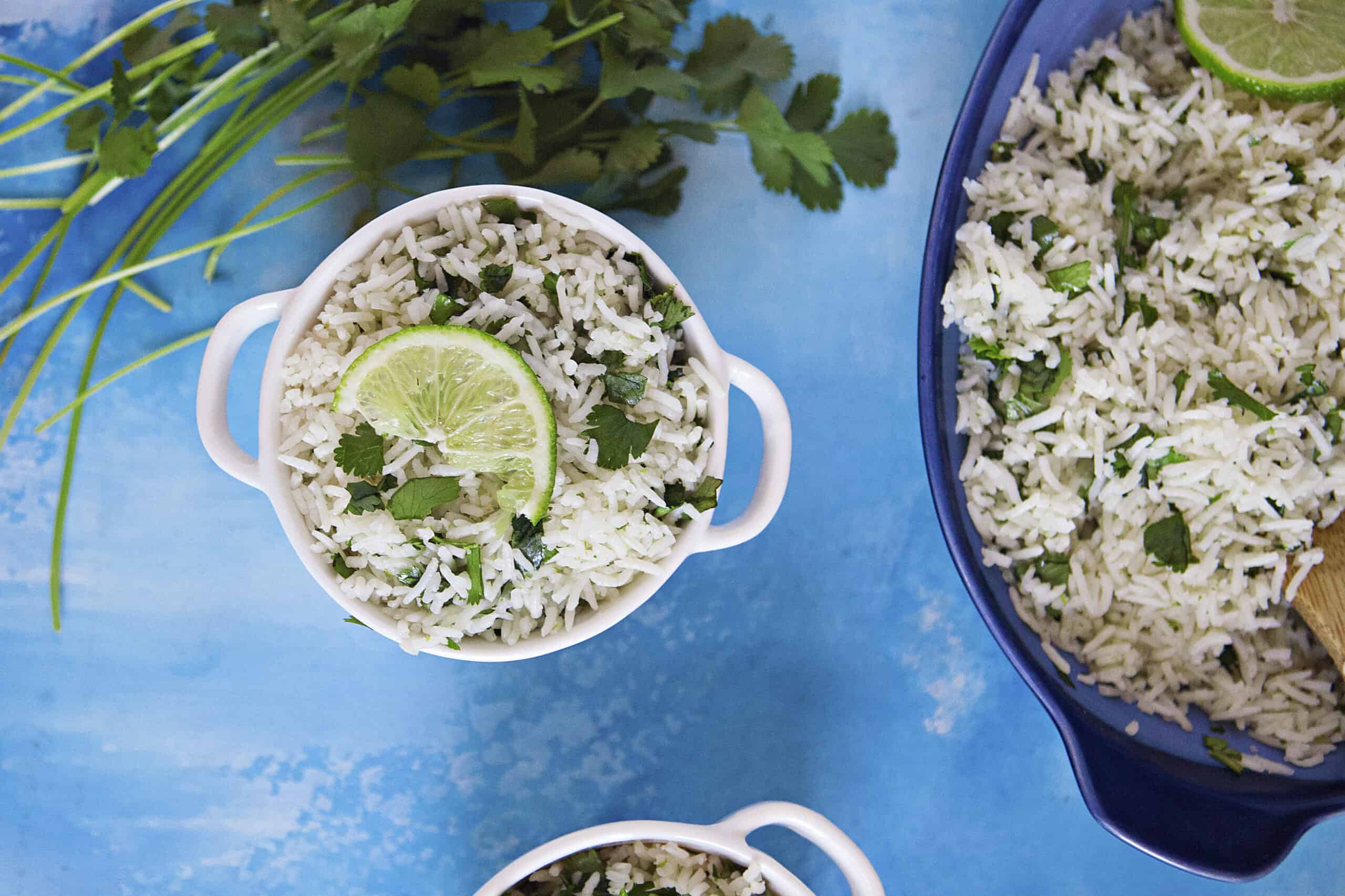 Fluffy lime-cilantro rice with a slice of fresh lime in a small bowl on a blue background with fresh cilantro.