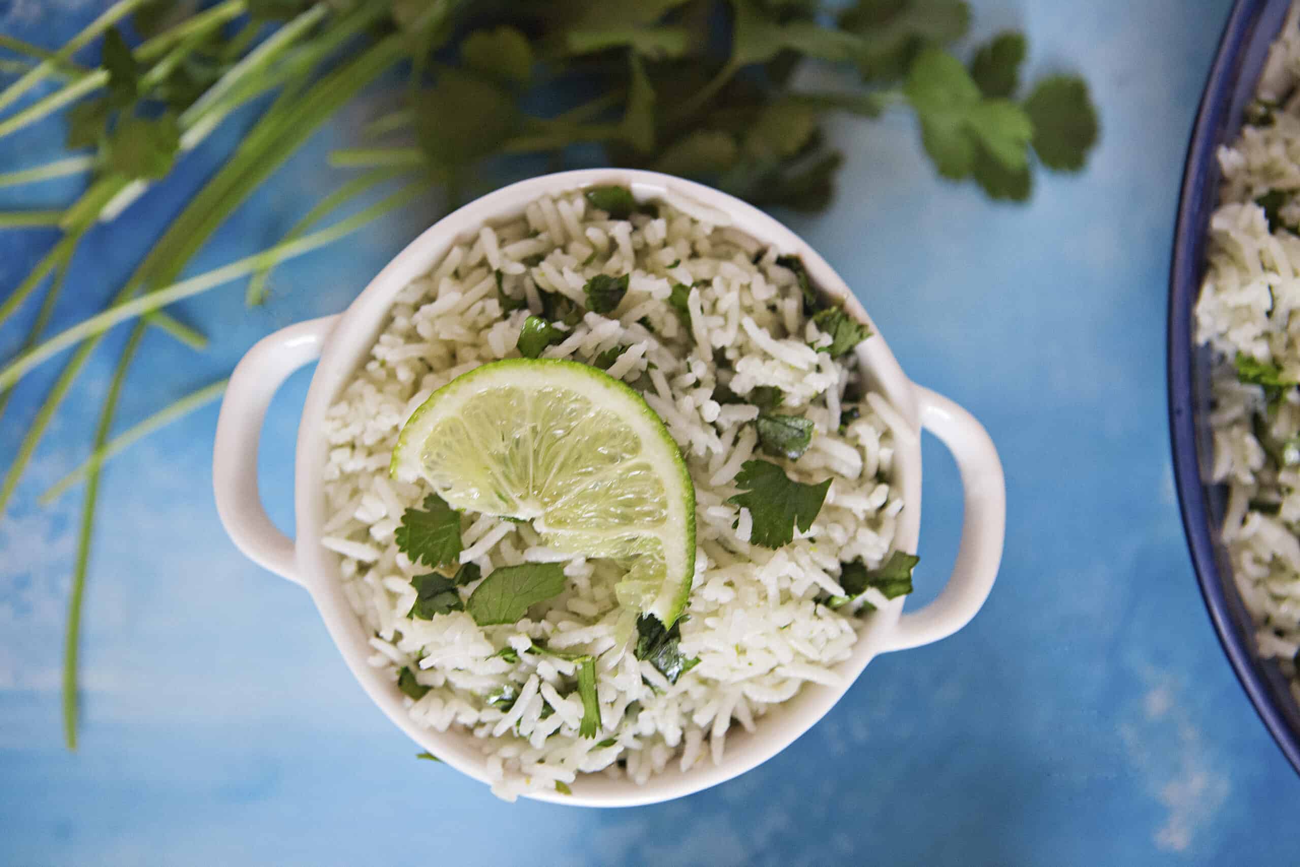 Fluffy lime-cilantro rice with a slice of fresh lime in a small bowl on a blue background with fresh cilantro.