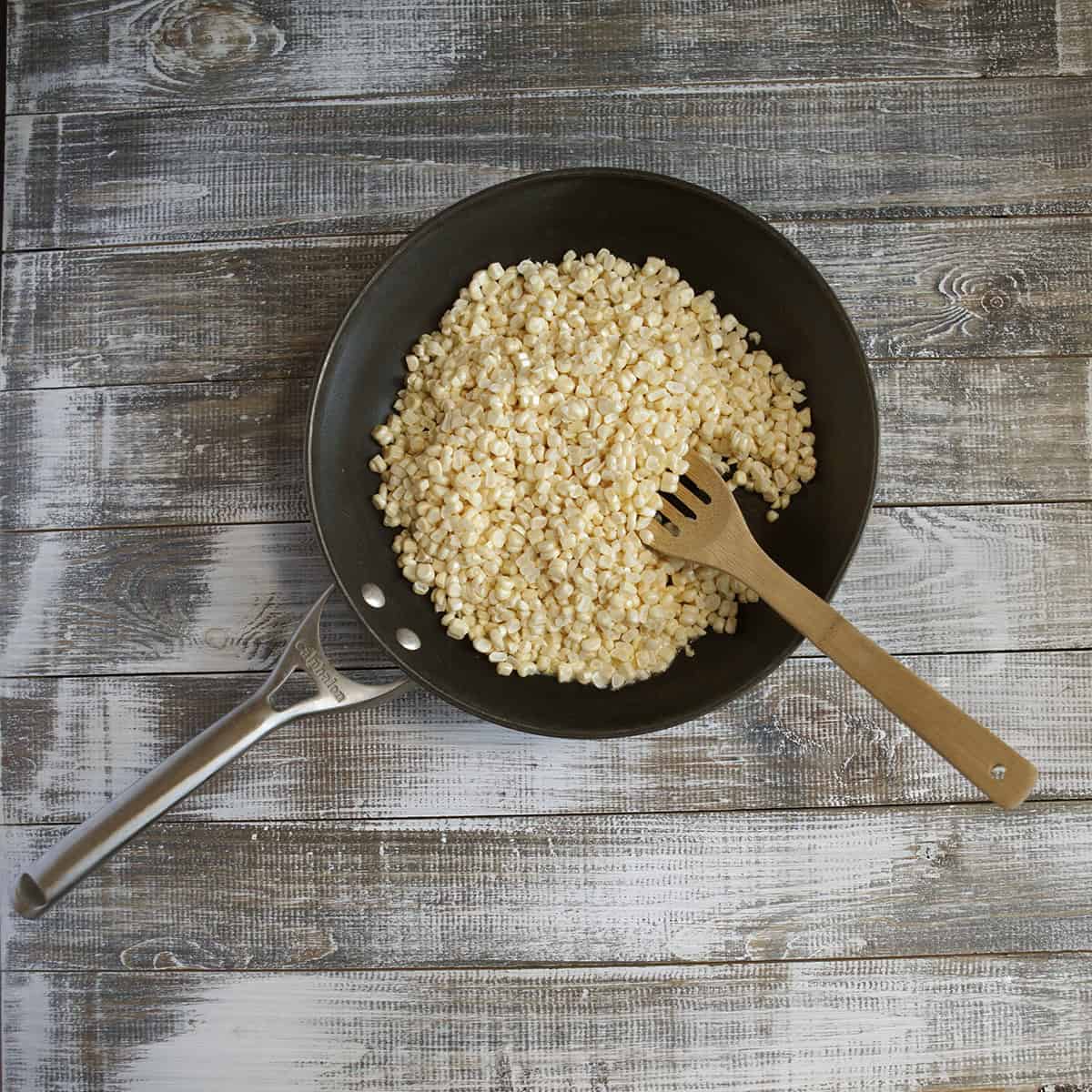 Corn kernels in a skillet with a wooden spoon.