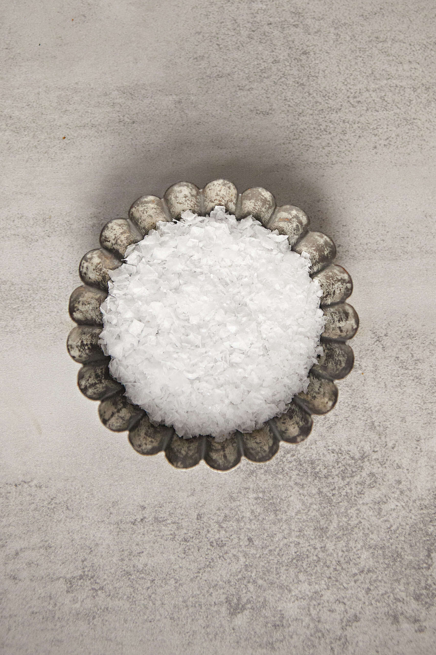 Flaky sea salt in a metal tart dish on a gray background.