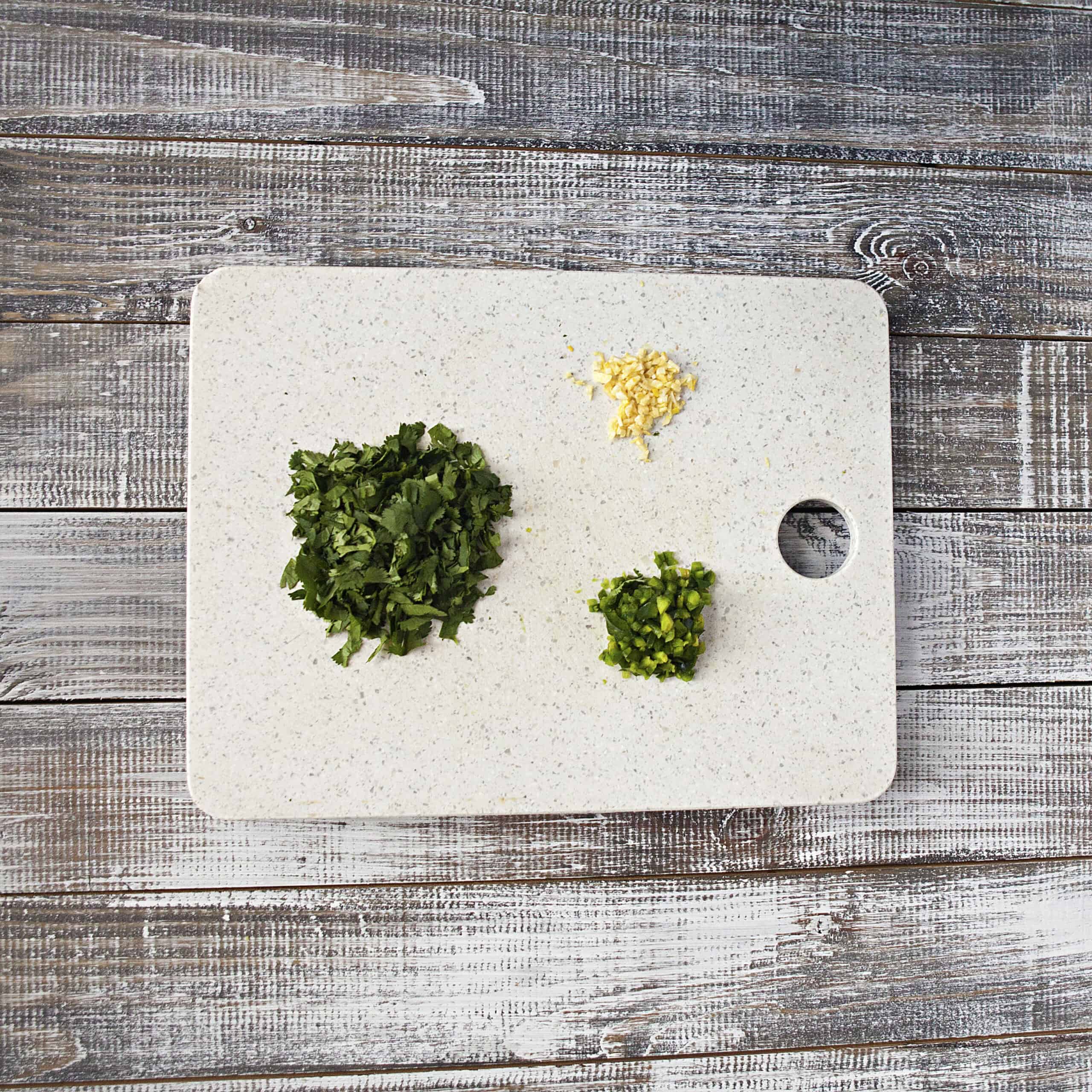 Minced garlic, diced jalapeno, and chopped cilantro on a white cutting board.