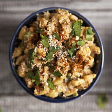 Mexican street corn (elote en vaso or esquites) in a blue ramekin topped with chopped cilantro, chili powder, and Cotija cheese.