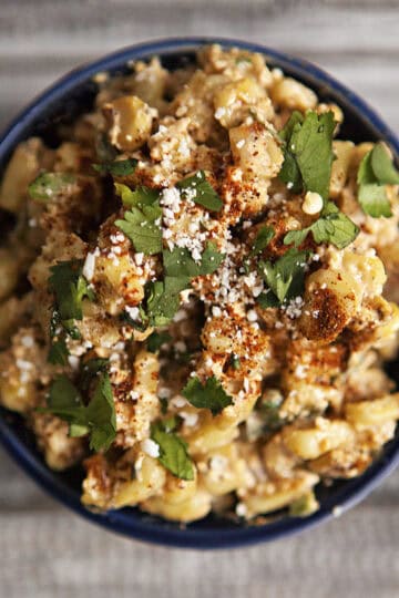 Mexican street corn (elote en vaso or esquites) in a blue ramekin topped with chopped cilantro, chili powder, and Cotija cheese.