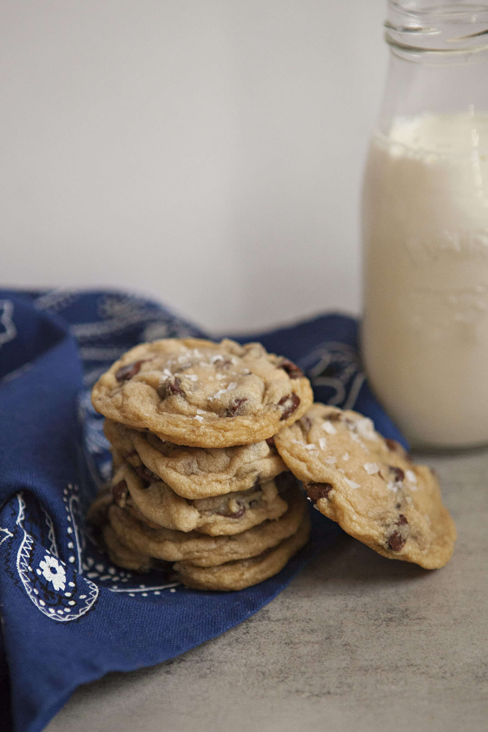 A stack of chocolate chip cookies on a blue kitchen towel next to a bottle of milk.