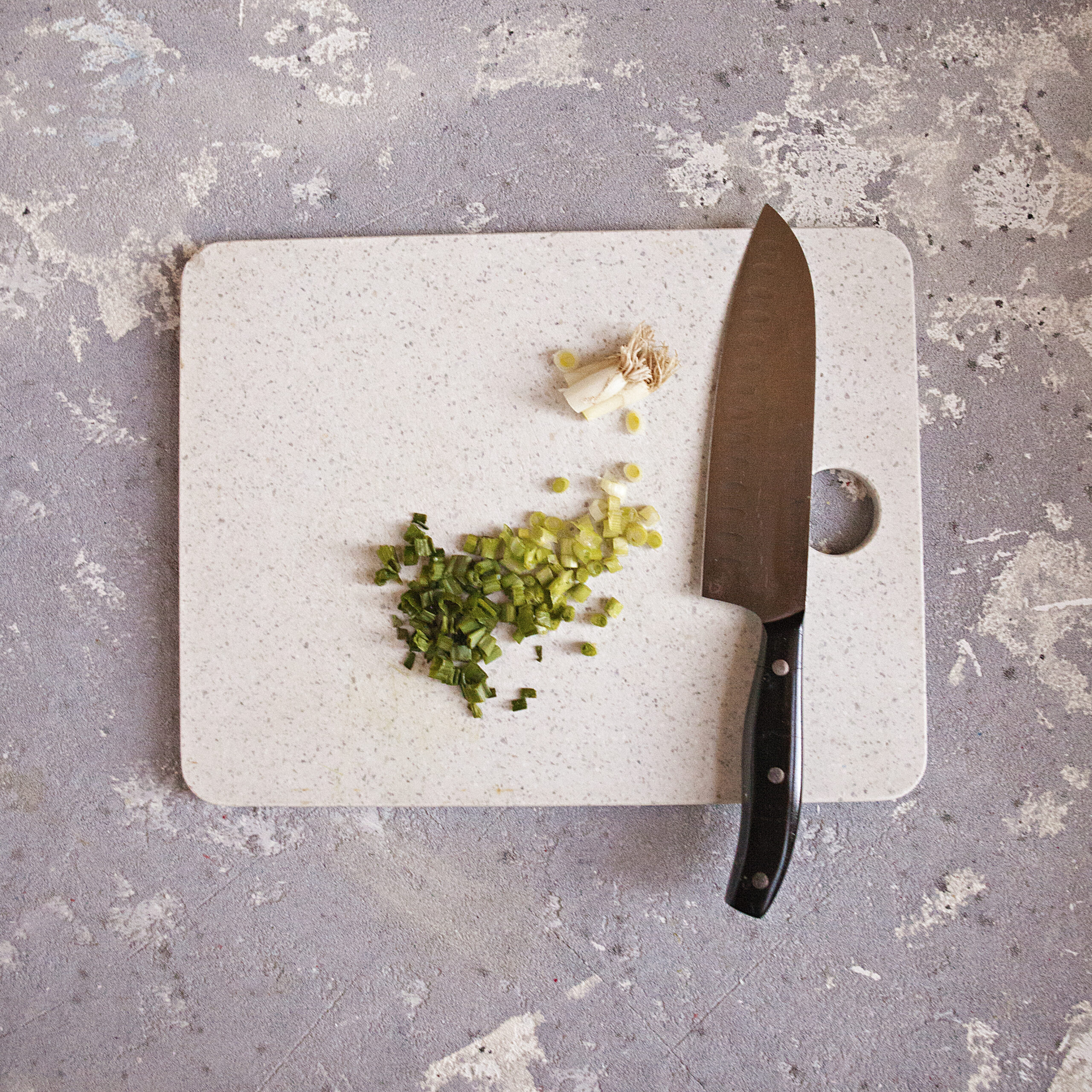 Chopped green onions on a white cutting board with a chef's knife.