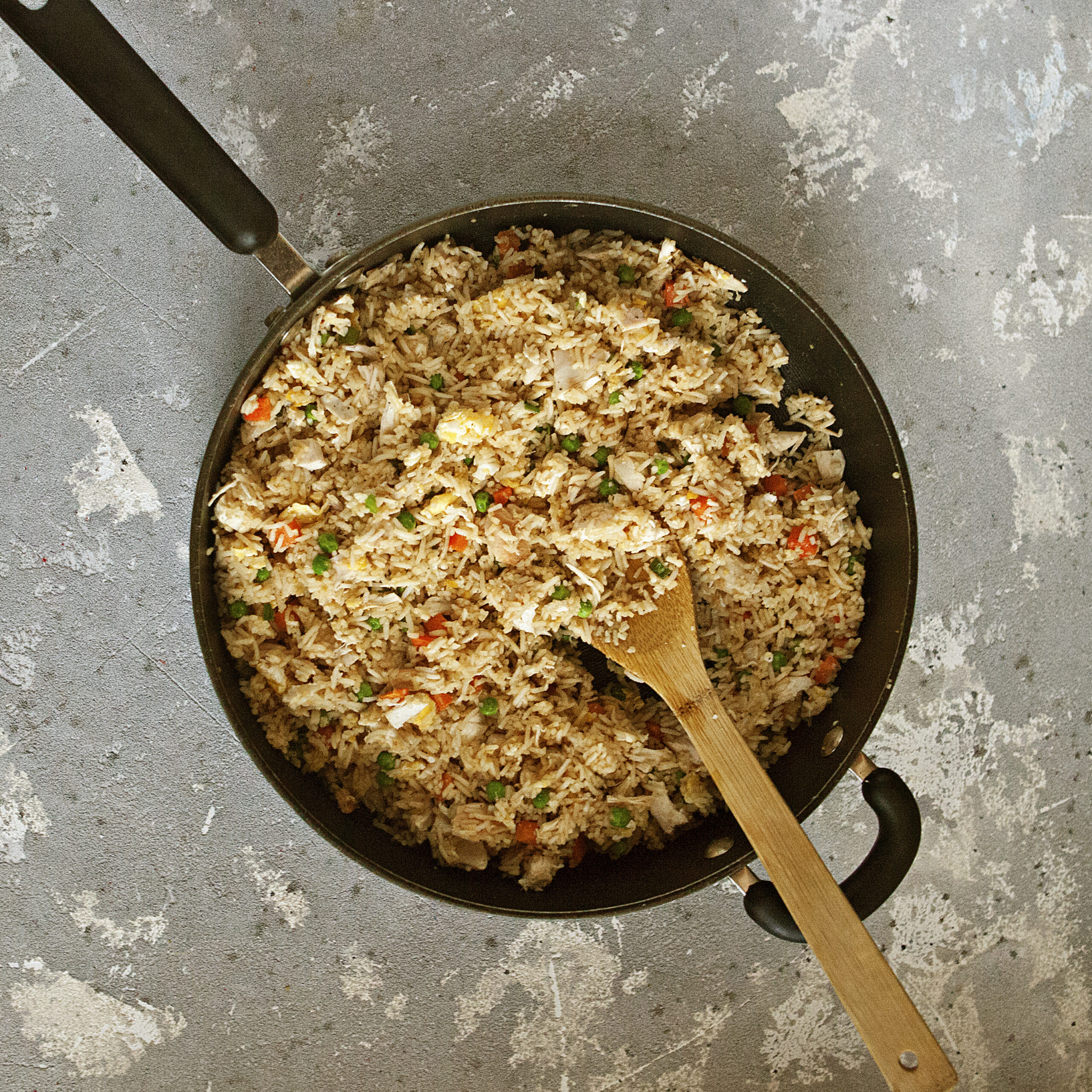 Chicken fried rice in a black skillet with a wooden spoon.