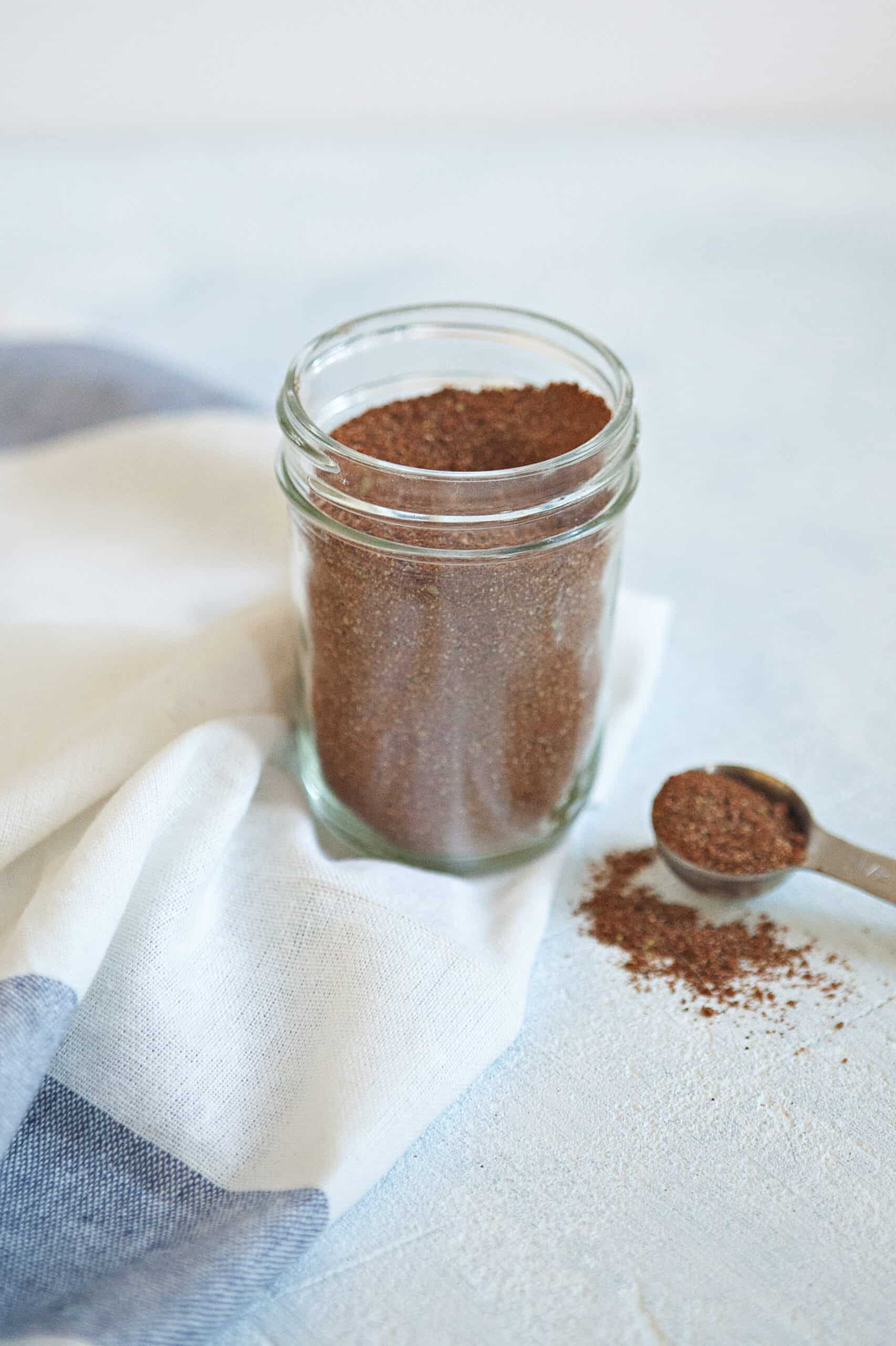 Homemade taco seasoning mix in a mason jar on a blue and white kitchen towel.