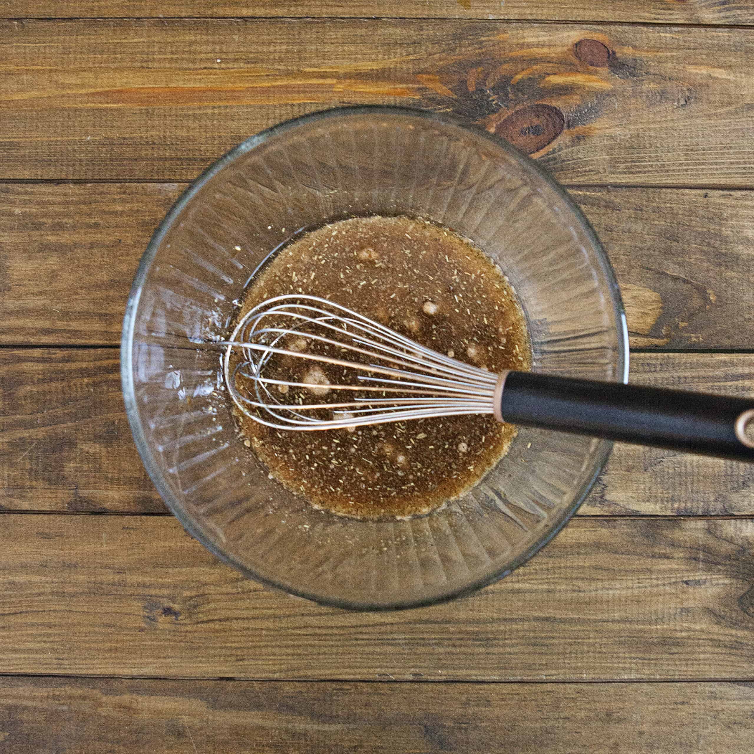 Balsamic marinade in an glass bowl with a whisk on a brown wooden table.