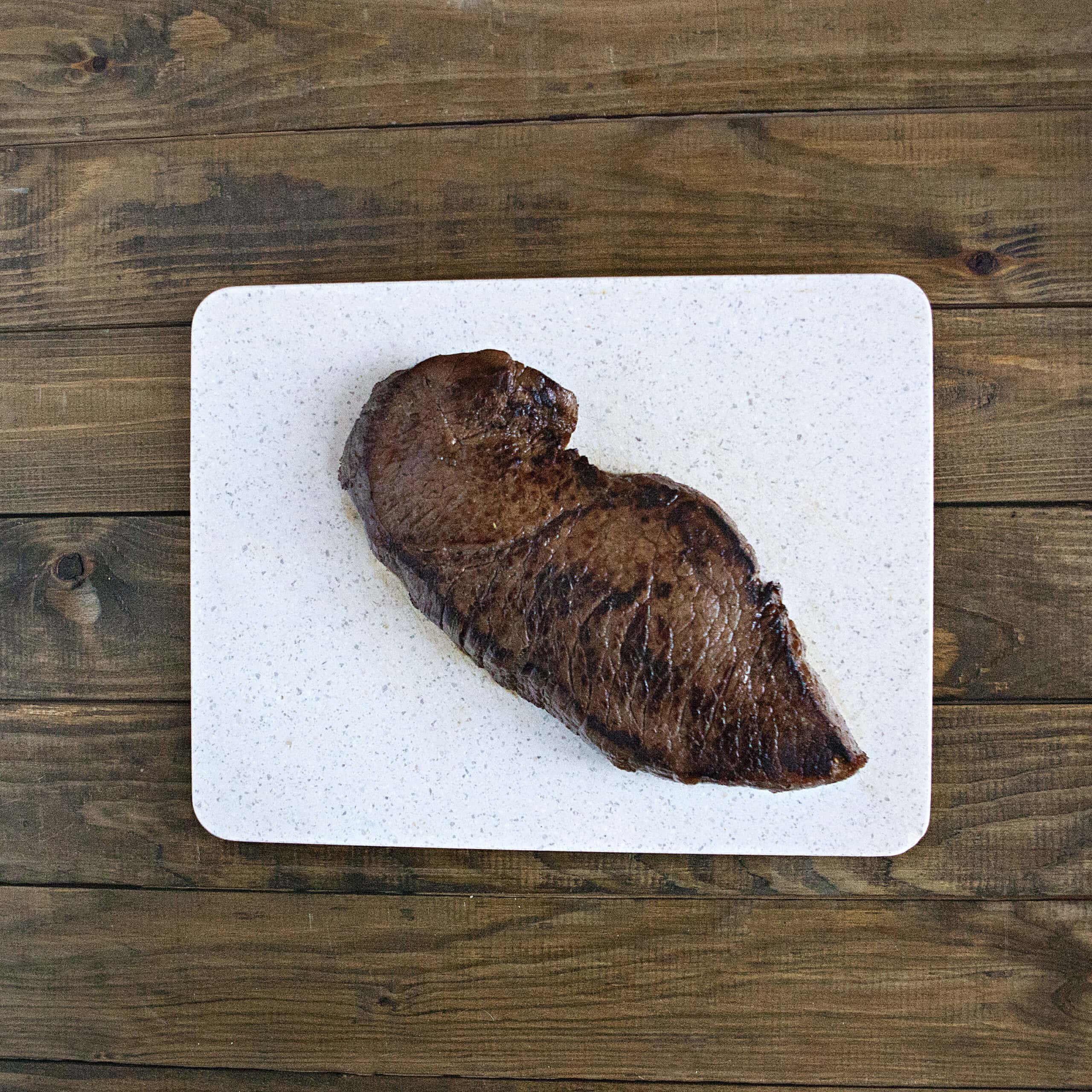 A cooked London broil steak on a cutting board on a brown wooden table.