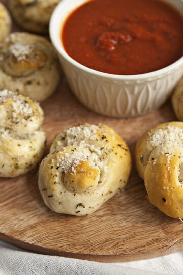 Buttery Parmesan garlic knots on a round serving tray with a white ramekin filled with marinara sauce.